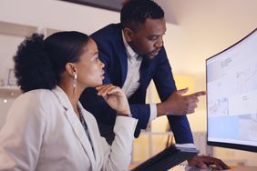 A business professional explaining something on a monitor to another person.
