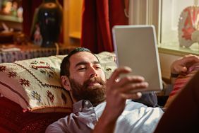 Man holding and reading an ereader while laying on a couch