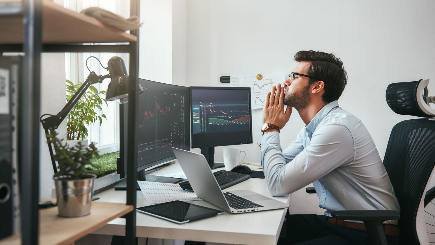 A concerned investor sitting at a desk monitoring market trading on computer screen