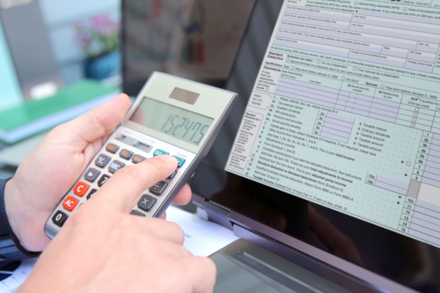 A taxpayer uses a calculator to arrive at a figure that they will input into a block on the tax form that appears on their laptop screen.