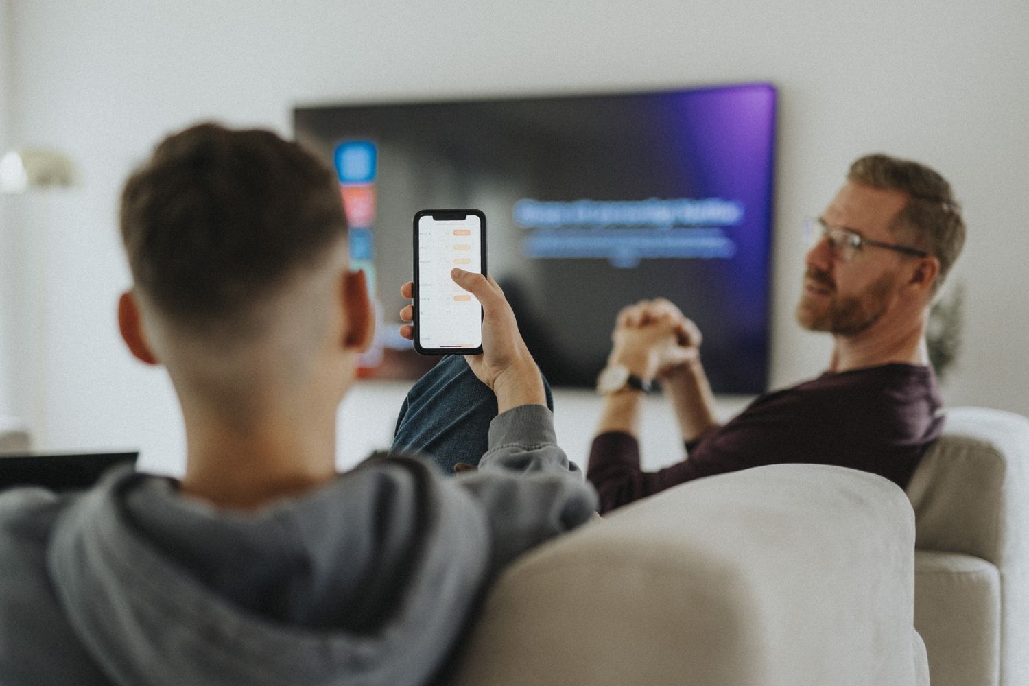 A teen uses a cellphone to take a picture of a television screen displaying a promotional web address.