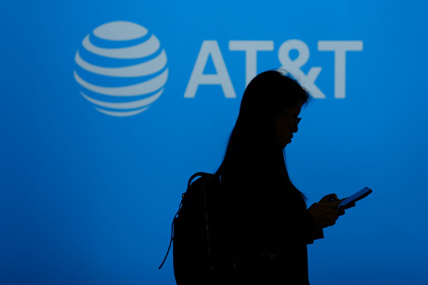 A silhouetted person walks past a sign bearing the AT&T logo. 