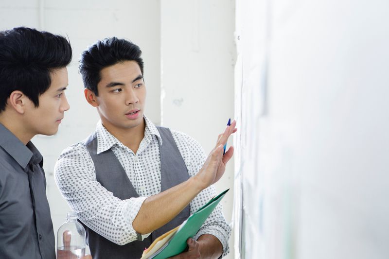 Two men stand in front of a wall of charts discussing business strategy.