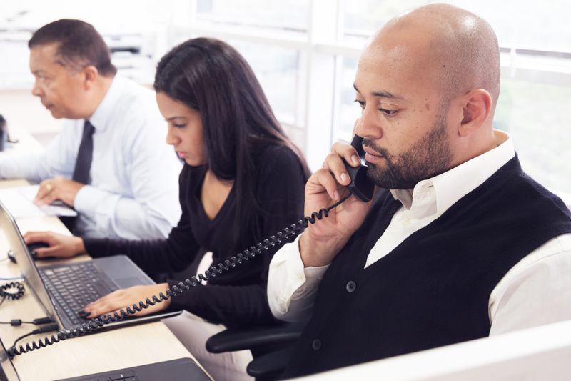 Traders sitting at trading desk. One is on the phone