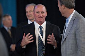 Greg Abel, wearing a suit and tie, speaks with a man at Berkshire Hathaway's annual meeting.