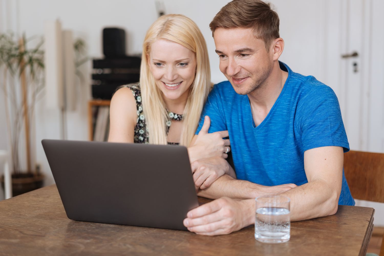 Young couple sitting at their kitchen table and looking happily together at a laptop