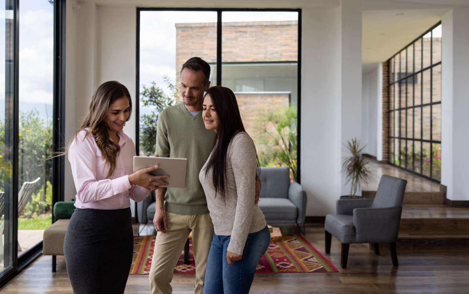 A man and a woman look at tablet held by a realtor in the living room of a house