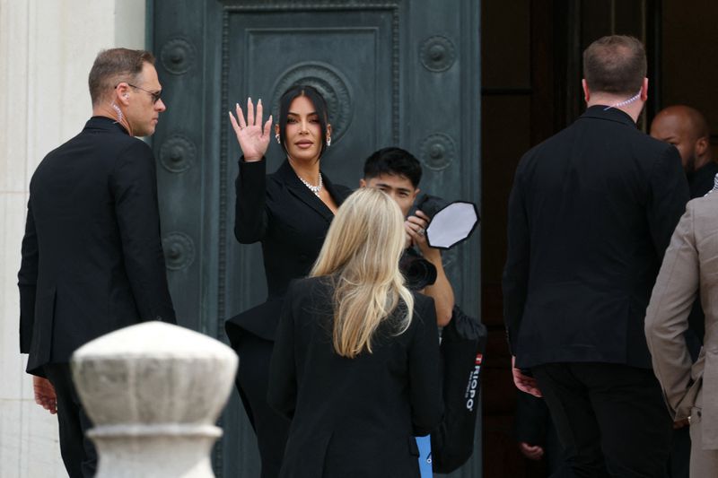 Kim Kardashian (center) waves as she arrives at the Assize Court for the trial during which she will testify over the 2016 robbery that saw her relieved of millions of dollars' worth of jewelry at gunpoint in Paris, on May 13, 2025.