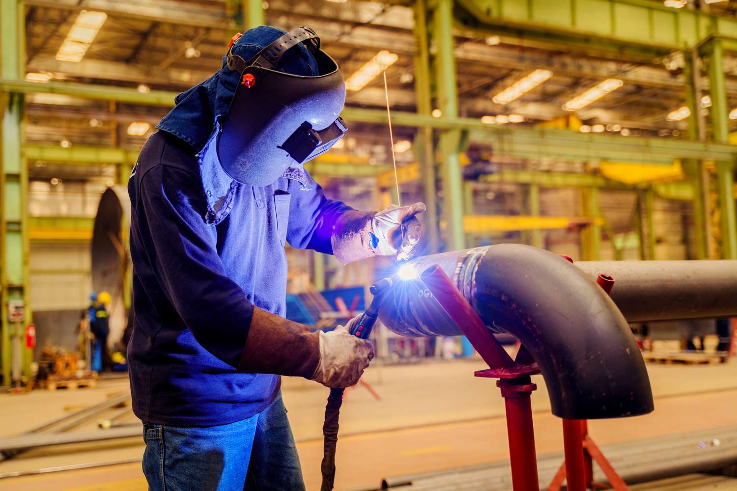 Male welder wearing helmet working with welding torch in factory.