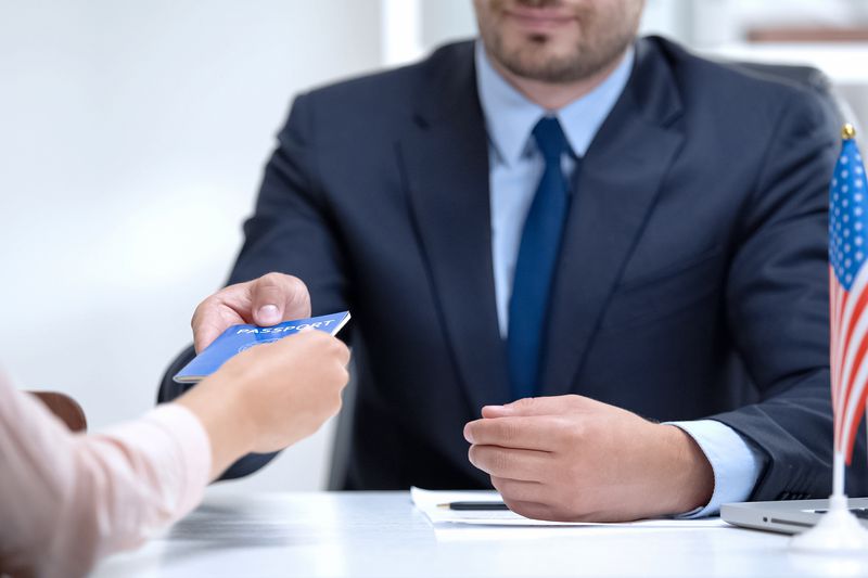 A man at a desk handing a passport to a woman in a close up of their hands. 