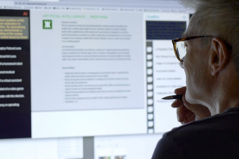 A mature white man looking at a computer monitor with an artificial intelligence chat window