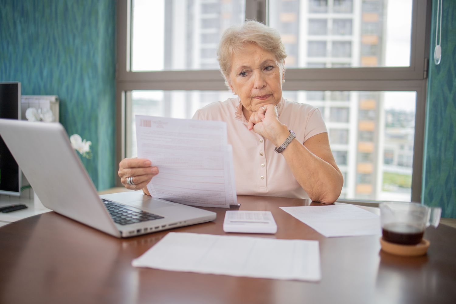 Older woman reading documents while sitting in front of a laptop and calculator