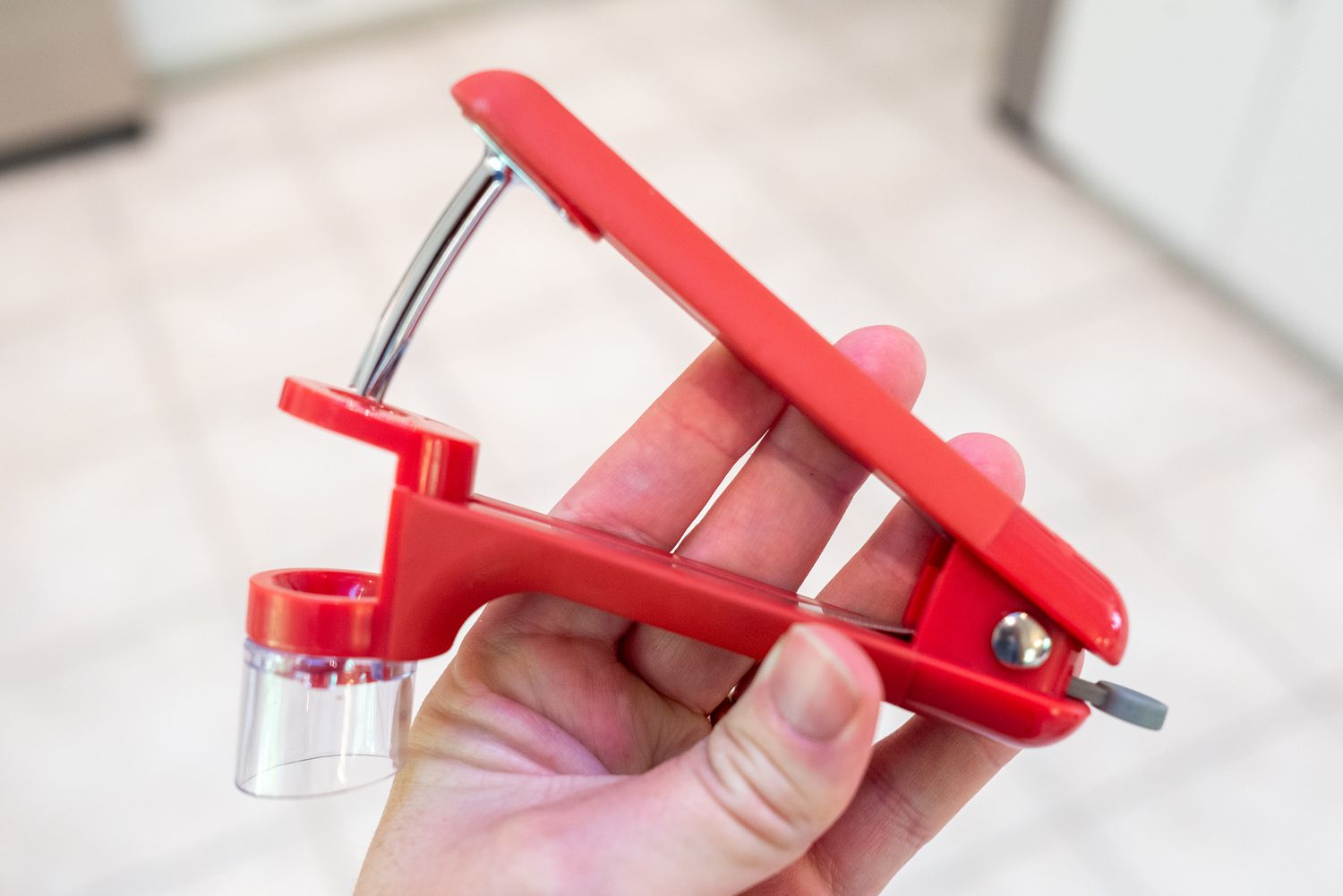 Close-up of a hand holding a red OXO Good Grips cherry pitter tool in a kitchen with tiled flooring, Lafayette, California, July 3, 2024