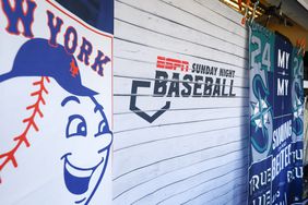 The ESPN Sunday Night Baseball logo is seen on a white wall, in between flags for the New York Mets and Seattle Mariners.