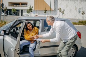 Young adult shaking hands to finalize a car loan to buy car for the first time at a dealer.