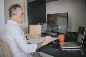 A retail trader sitting at him computer with an open laptop also on the desk