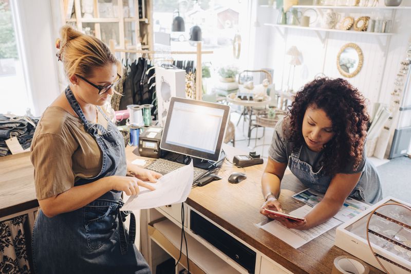 Colleagues discussing financial receipt with digital tablet at checkout counter in store