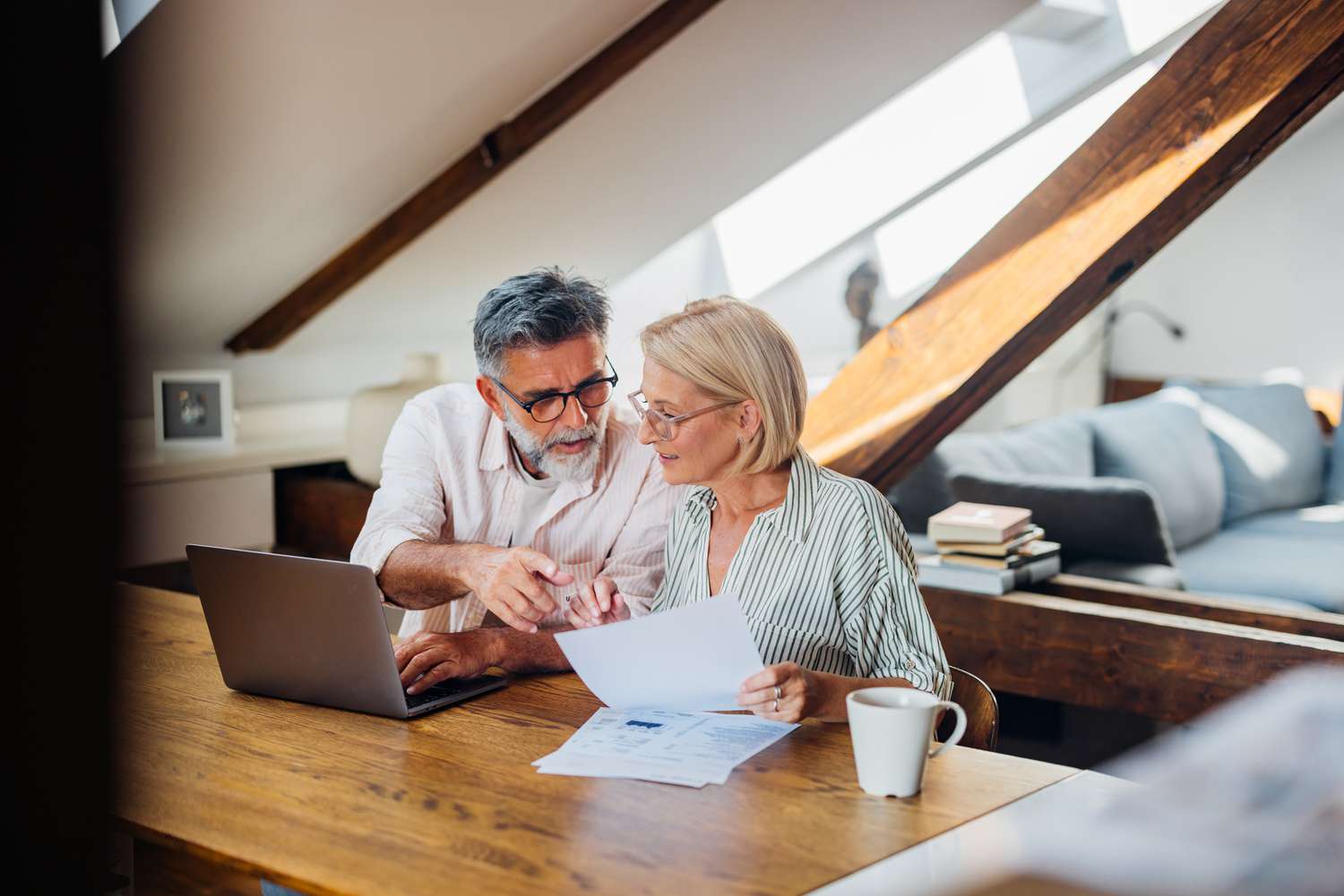Senior couple sitting at a desk in their home office, working on documents together using a laptop.