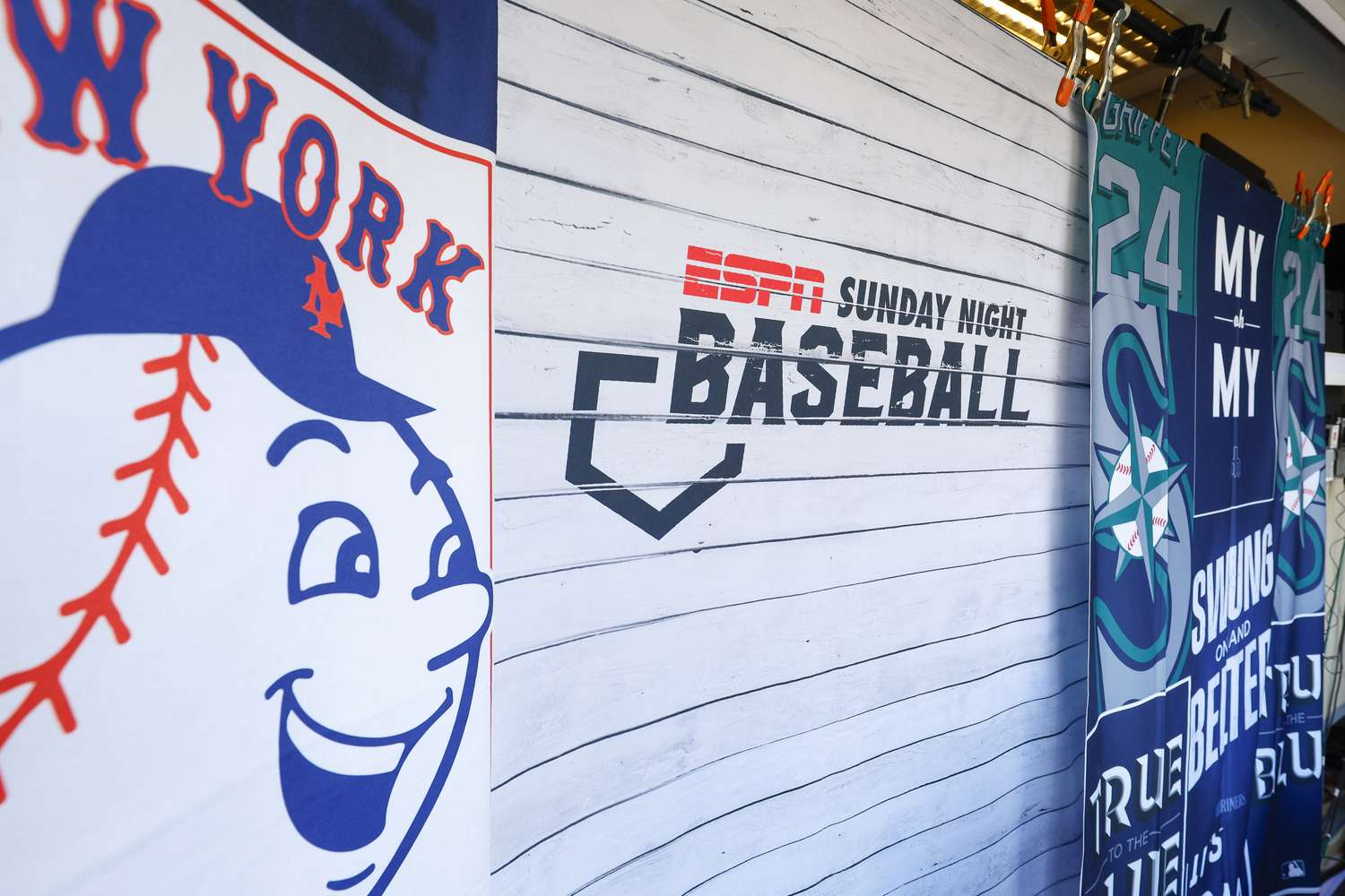 The ESPN Sunday Night Baseball logo is seen on a white wall, in between flags for the New York Mets and Seattle Mariners.