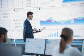 A senior financial analyst reviewing information and reports on big digital screen in modern monitoring office.