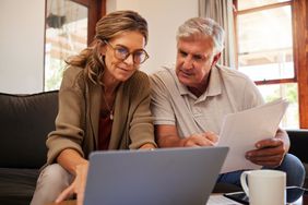Older couple sitting on their sofa as they look at mortgage documents and a laptop