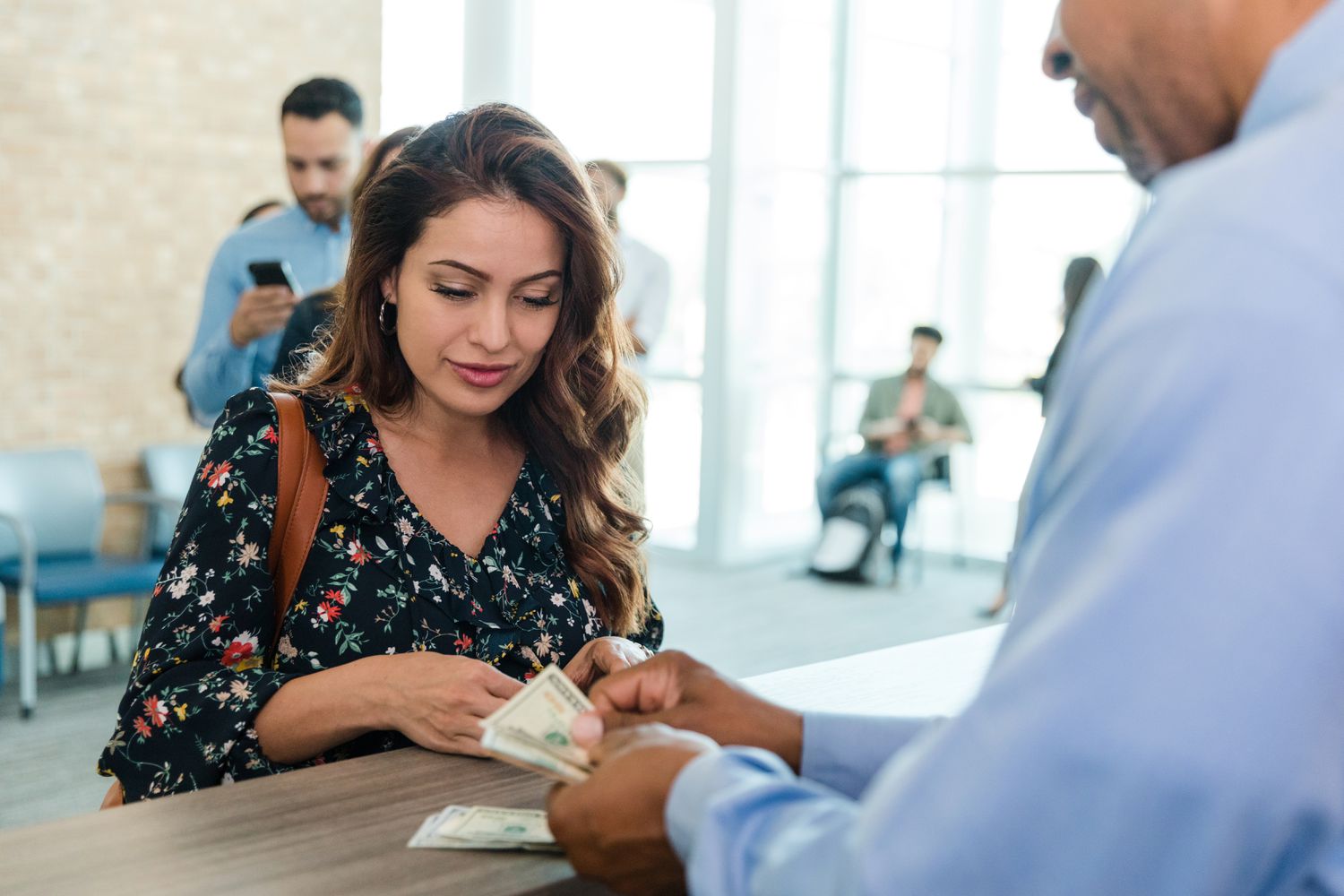 Woman at bank watching bank teller in front of her counting money that she withdrew from her account.