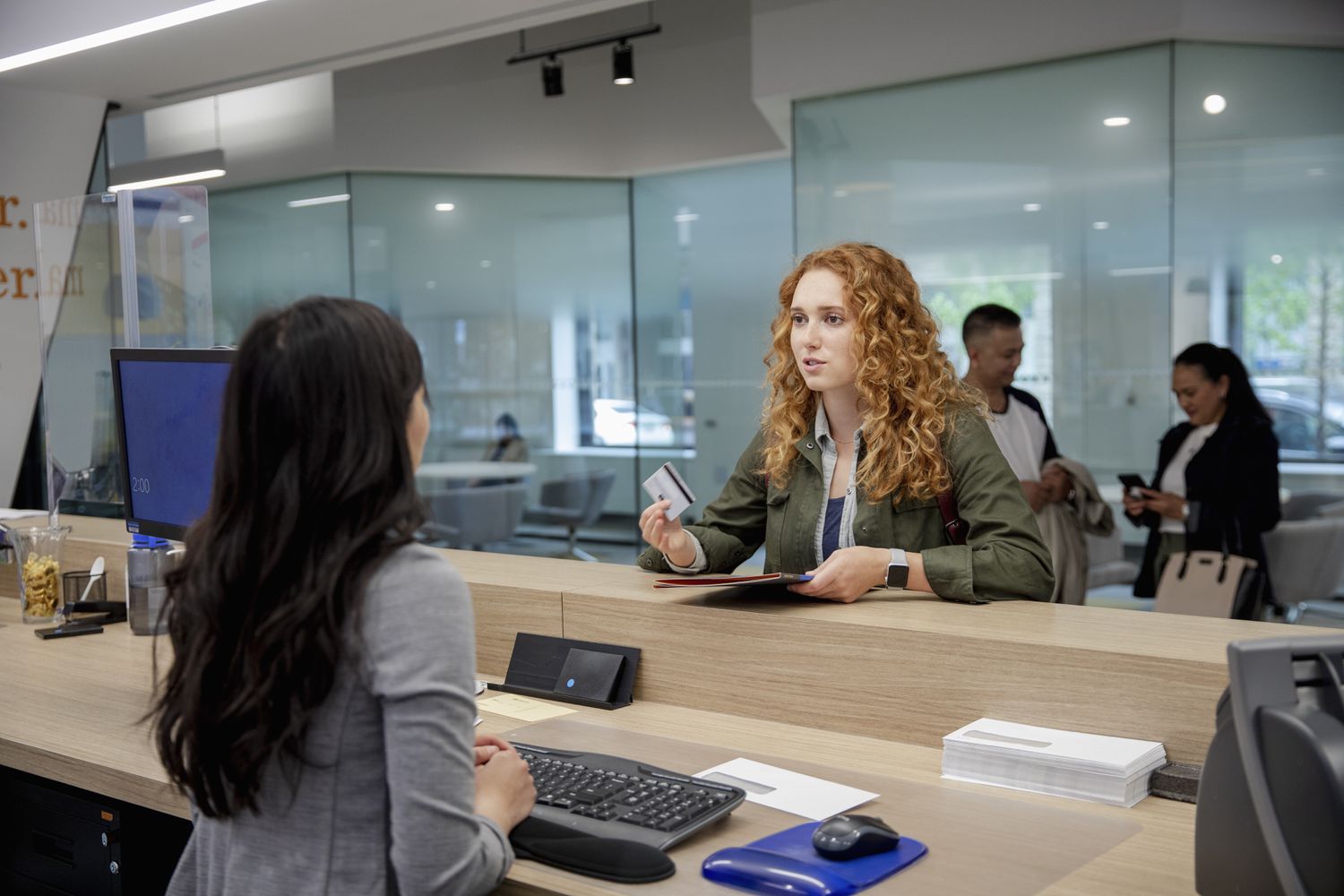 A woman with a card talks with a bank teller