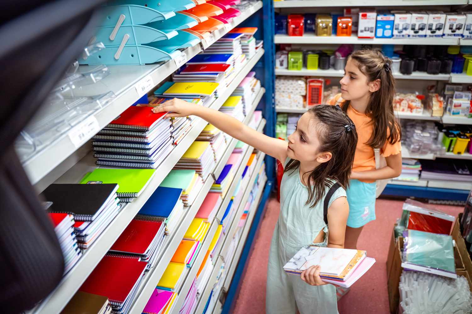 Two school-aged children sort through notebooks and folders during back to school shopping. 