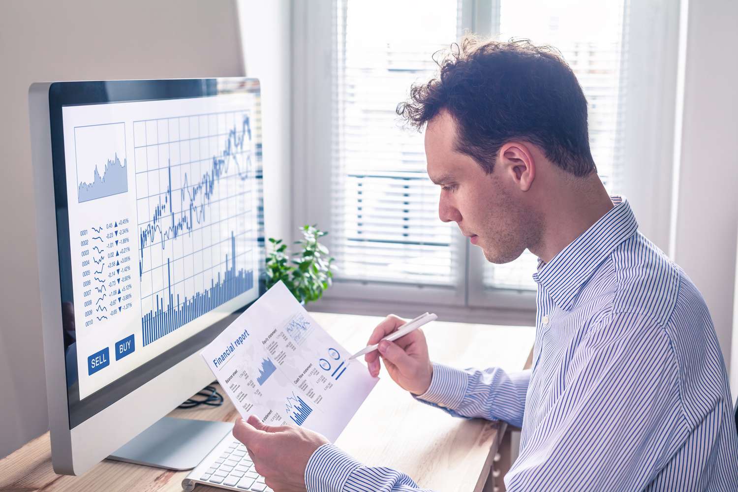 A trader sits in front of a computer and reads a printout of a StockCharts Technical Rate data for a security they follow. 