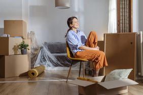 Cheerful happy young woman enjoying in her new apartment. She is surrounded by moving boxes and belongings
