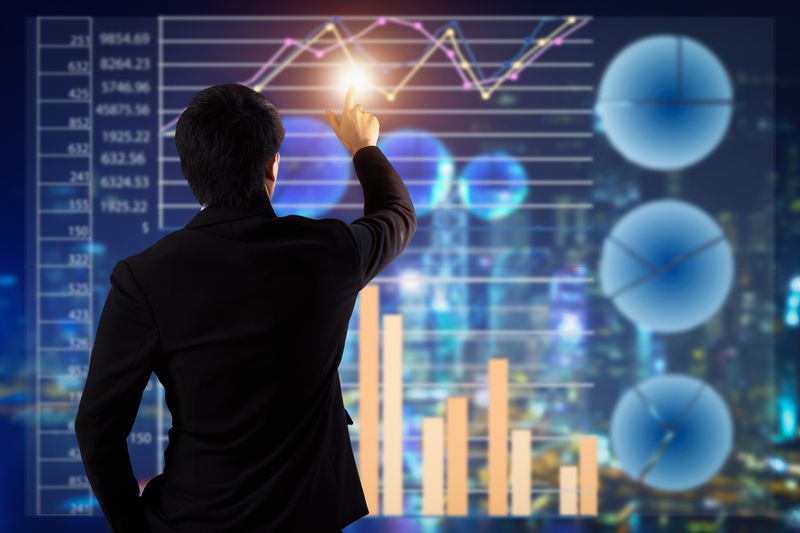 A businessman pointing a monitor with 3D charts and graphs.