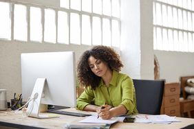 A woman in her office makes notes on a piece of paper