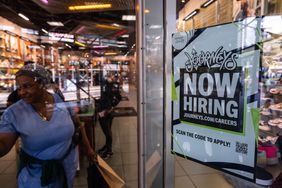 Journeys store entrance with a 'Now Hiring' sign, woman walking in the background, other store visitors visible