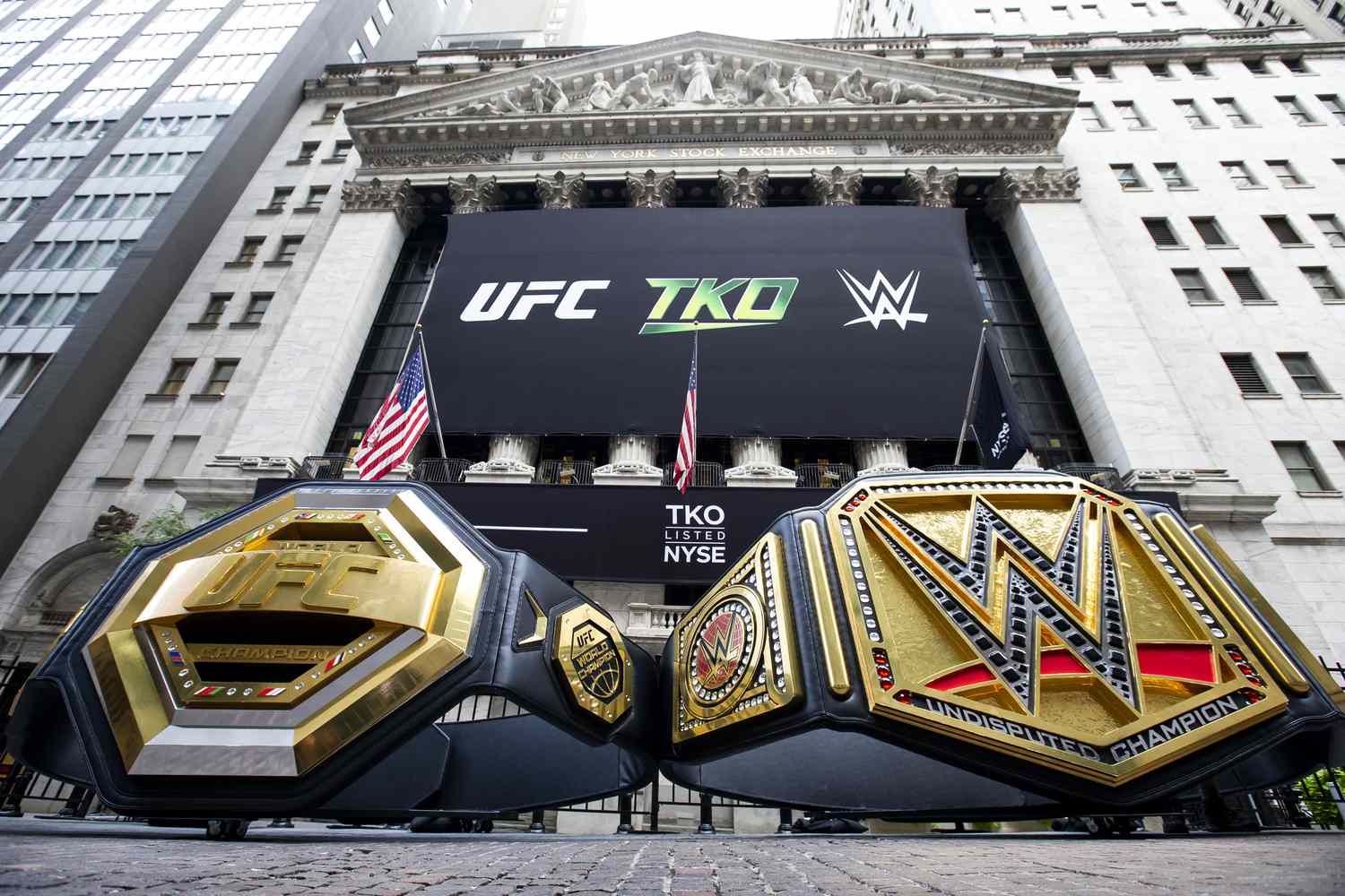 A pair of large black and gold championship belts with the UFC and WWE logo sit outside the New York Stock Exchange.