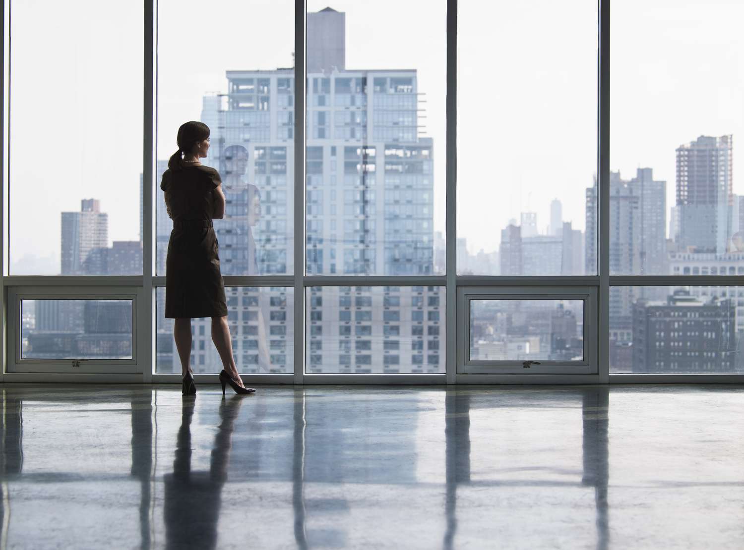 Woman standing in front of a floor to ceiling window looking at the skyline