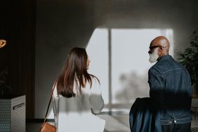 Conceptual image of a woman and man, separated by the shadows on the wall, yet standing next to one another.