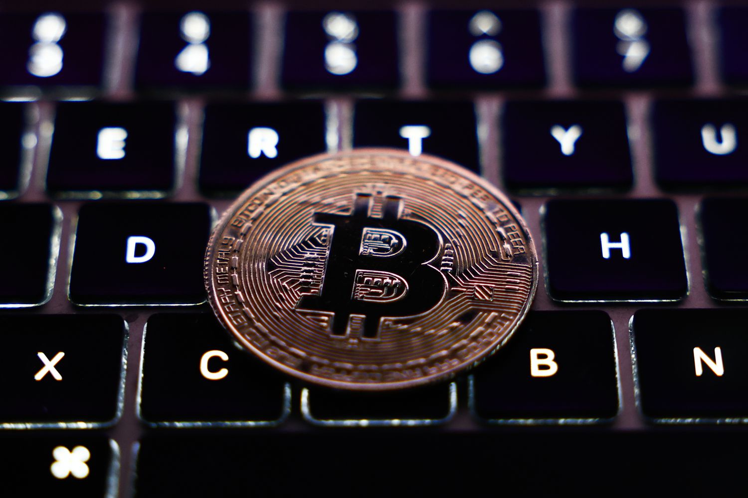 A physical representation of the Bitcoin cryptocurrency sits on a laptop keyboard.