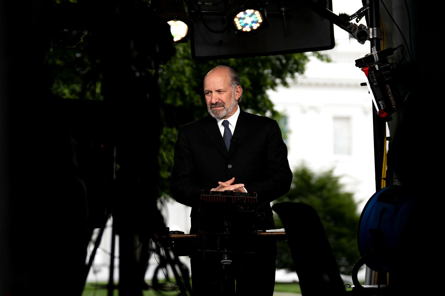 Howard Lutnick stands with his finders interlaced in front of his stomach. Cameras and lights surround him on the White House lawn.