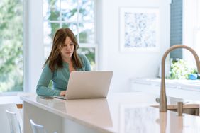 An investor uses their laptop on the kitchen countertop to look at the performance of their Roth IRA account. 