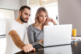 Couple in their 20s or 30s in their kitchen and looking at mortgage rates on a laptop