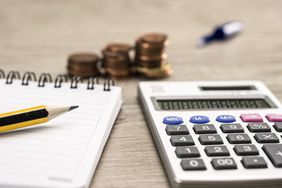 Pencil lying on top of a note pad, next to a calculator and stacks of pennies. 