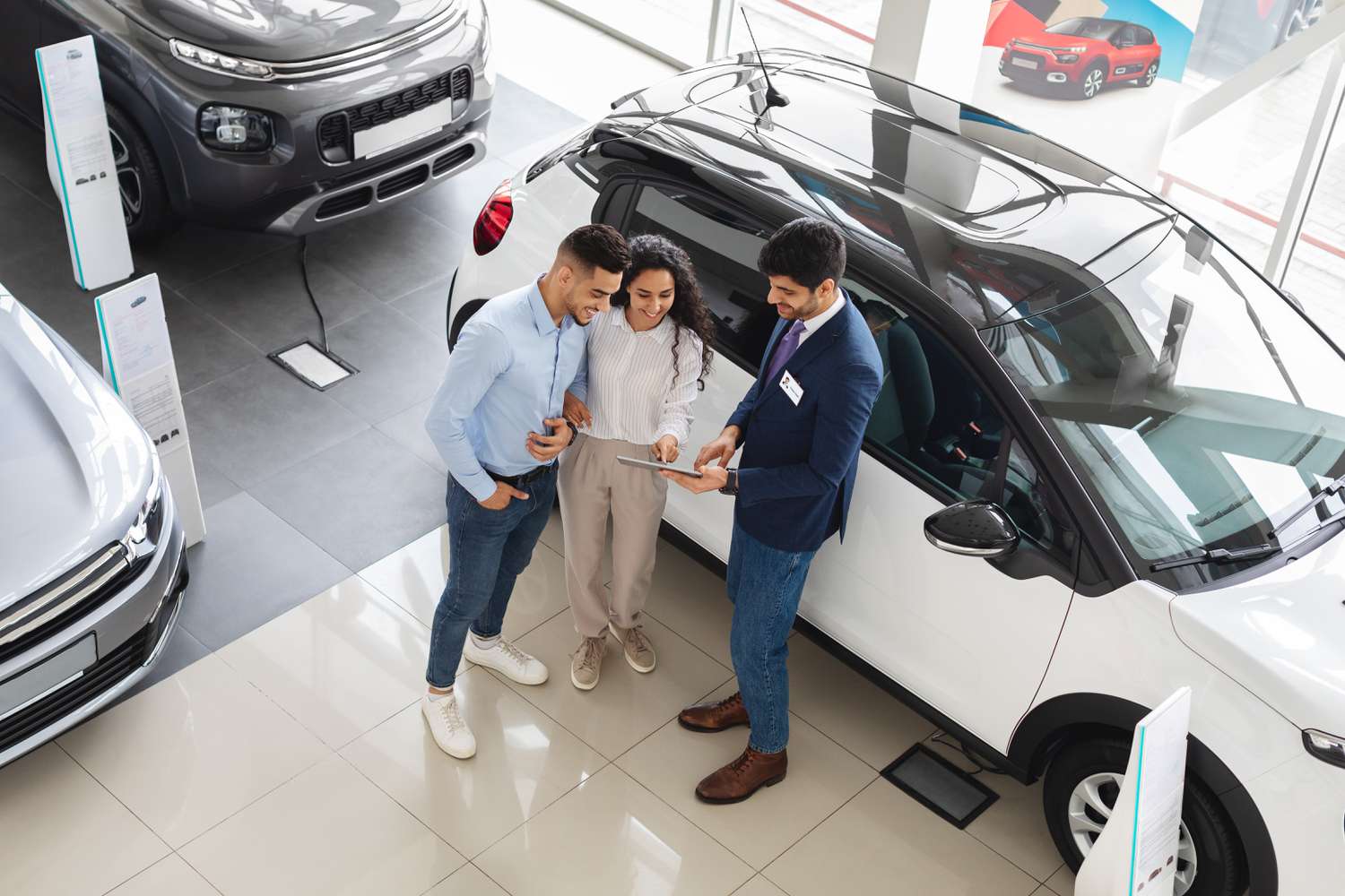 A couple look at a tablet being held by a car salesman inside a dealership. 