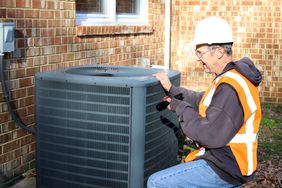 Maintenance worker looking at air conditioner unit outside home