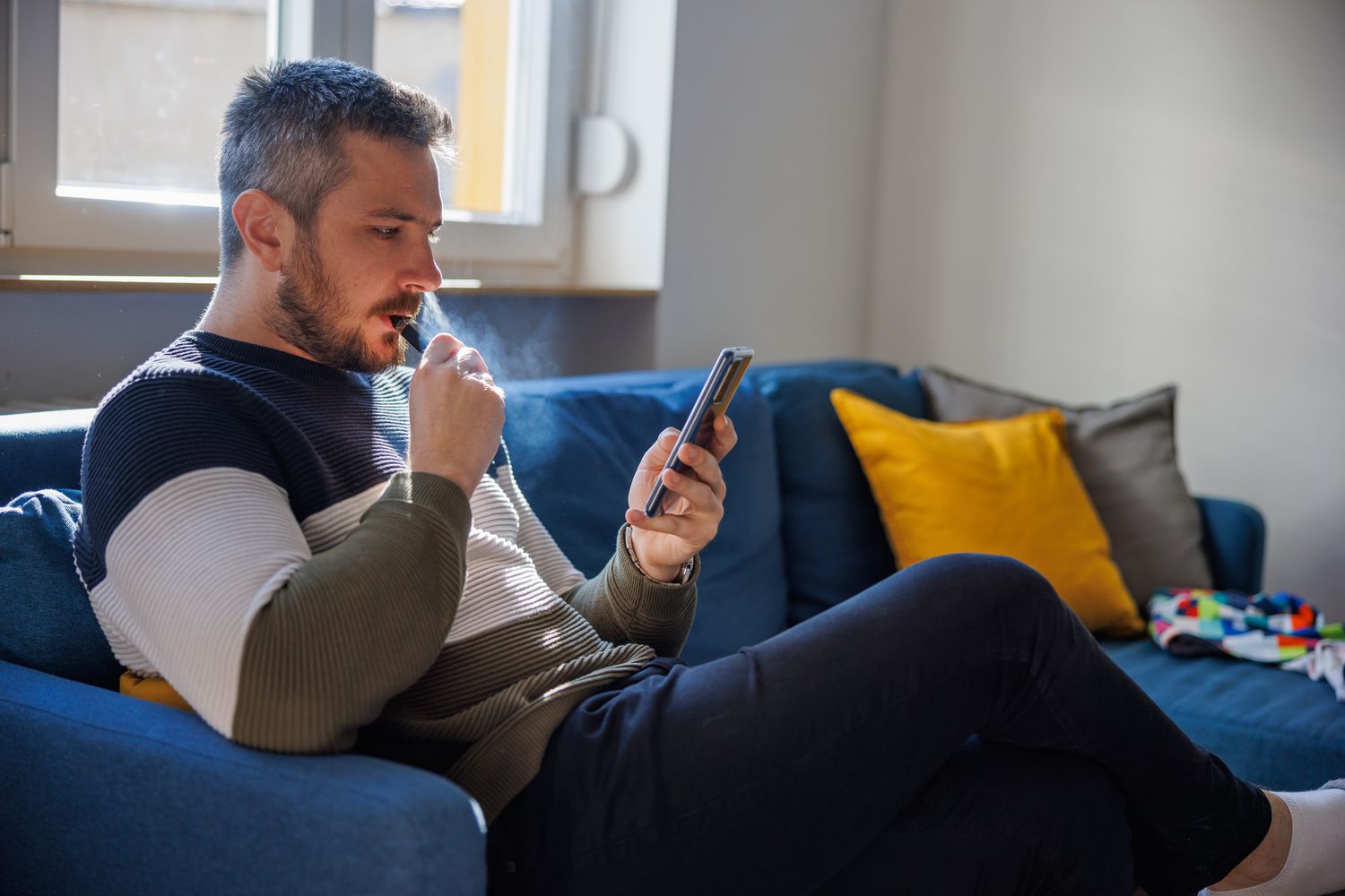 The unitholder of a master limited partnership investment sits on their sofa and reviews their investment using a cellphone.