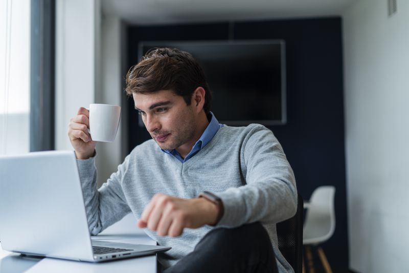 Young man sitting at his desk and looking serious at financial information on a laptop