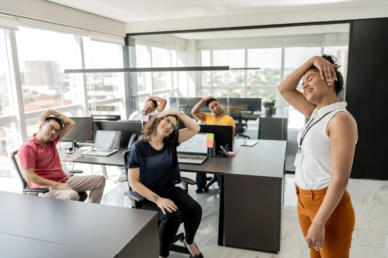 Workers do stretching exercises while sitting in office chairs at their workstations as part of the wellness program.