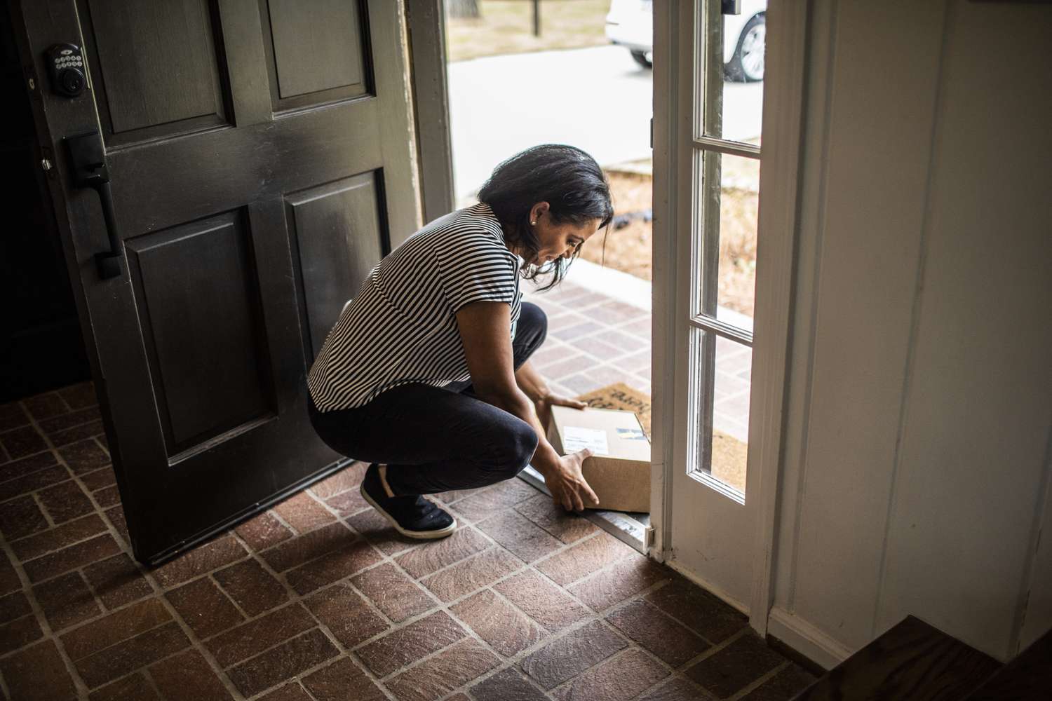 A woman picks up a package left outside her home's front door. 