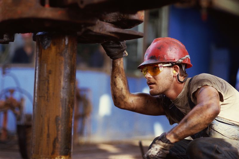 Oil Rig Worker Wearing Hard Hat and Safety Goggles, Checking Drill