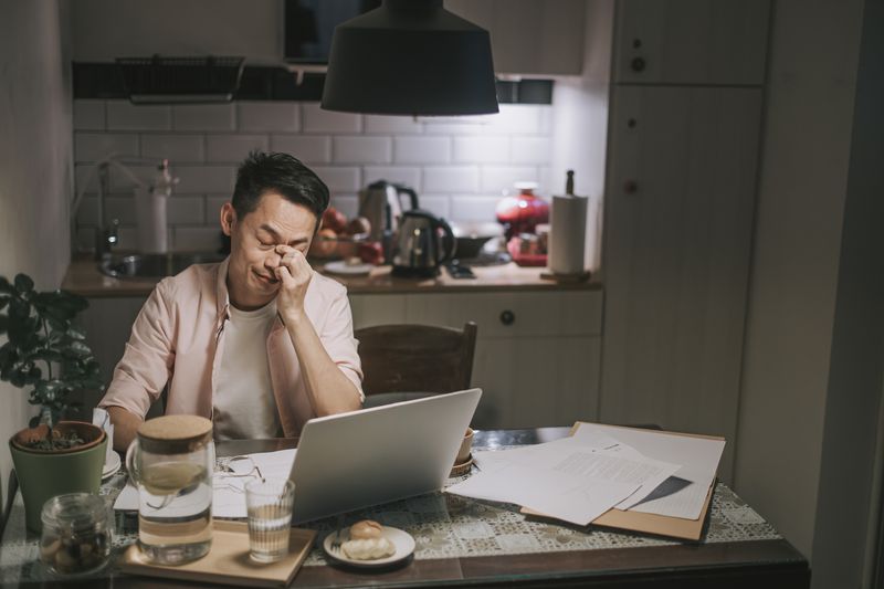 Asian male worries about his debt while sitting in the kitchen at night