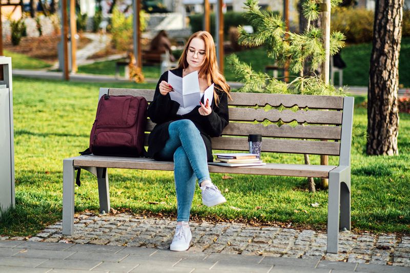 Young student girl in glasses and with laptop and books reading letter outdoors.